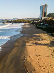 イタペマにあるSuíte com vista para montanhas no Blue Sea Hotel, beira-mar+lazer completoの砂浜を歩く二人