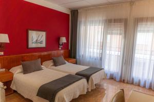 two beds in a room with red walls and windows at Hostal Regina in Blanes