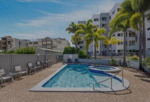 a swimming pool with chairs and trees and buildings at On The River Apartments in Maroochydore