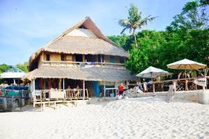 a hut on the beach with people sitting in front of it at Santai Guesthouse Balangan in Uluwatu