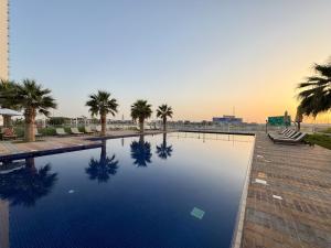 Modern High-Floor 1BR Apartment with Balcony, Pool Access & Golf Course View, Up to 4 Guests, by Stayfinity في دبي: مسبح بالنخيل وغروب الشمس