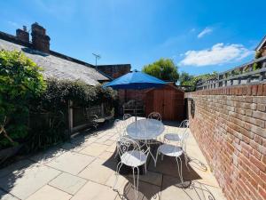 un patio avec une table, des chaises et un parasol dans l'établissement Bridewell Cottage in the heart of Tenterden - Pass The Keys, à Tenterden