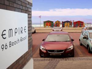 un coche rojo estacionado en un estacionamiento cerca de la playa en The Waves Empire Apartment, en Muizenberg
