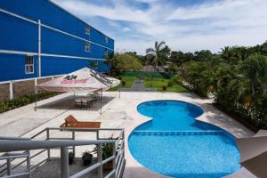 a swimming pool next to a blue building with an umbrella at Capital O Hotel Los Caracoles, Acapulco in Acapulco