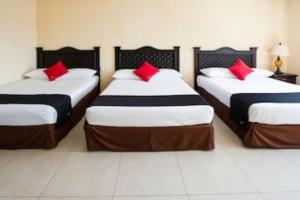 three beds in a room with red pillows on them at Capital O Hotel Los Caracoles, Acapulco in Acapulco