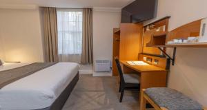 een kleine hotelkamer met een bed en een bureau bij Best Western Corona Hotel in Londen