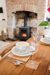 einen Tisch mit 2 Gläsern und Tellern sowie einen Kamin in der Unterkunft Sweetheart Cottage - Cosy 2 Bed in The Cotswolds! in Swalcliffe
