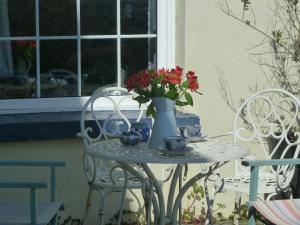 a table with a vase of flowers and two chairs at Bell Ringers Cottage in Loddiswell