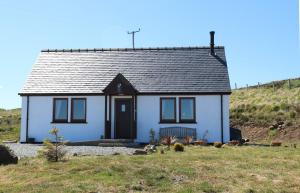 a white house with a black door on a hill at Taigh na Laige in Flashader
