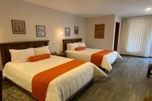 Habitación de hotel con 2 camas con sábanas de color naranja y blanco en Collection O Hotel La Huerta Golf & Hotel, Cholula, en Cholula