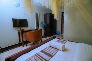 ジンジャにあるThe Mansion Hotel Jinjaのベッドと机とテレビのある寝室