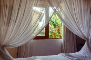 a bedroom with white curtains and a window at Pausa Trancoso in Trancoso