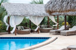 a resort swimming pool with chairs and a thatched umbrella at Pousada Aruana in Canoa Quebrada