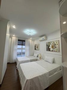 a bedroom with two beds with white sheets and a window at HOMESTAY CAO CẤP TẠI NEWLIFE HẠ LONG 2PN in Ha Long