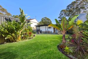 une cour avec de l'herbe et des arbres verdoyants et une maison dans l'établissement Piccolo Cottage - Firepit - 4 Mins Walk to Beach, à Callala Beach