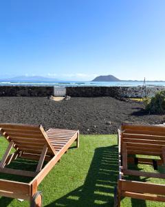 two wooden benches sitting on the grass near the ocean at BeachFront Villa - La Casa del Mar in Corralejo
