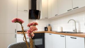a kitchen with white cabinets and pink flowers in a vase at Na Sudeckim Szlaku by LibertaRent in Mieroszów +6 photos