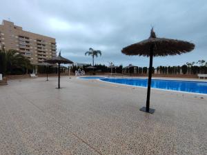 3 parasols en paille en face d'une piscine dans l'établissement EDIFICIO JARDINES DEL MAR II en Magic World, à El Borseral