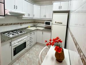 a kitchen with white cabinets and red flowers on a table at Apartamentos Mar Bella Segur de Calafell 3000 in Segur de Calafell