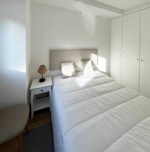 a white bedroom with a bed and a night stand at Casinha PP Guest House in Coimbra