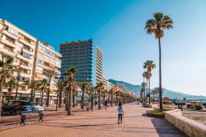 Eine Frau, die eine Straße mit Palmen und Gebäuden entlang geht. in der Unterkunft One bedroom apartment central Fuengirola in Santa Fe de los Boliches