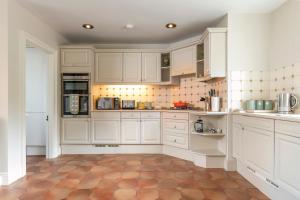 a kitchen with white cabinets and a tiled floor at Laundry Cottage in High Legh