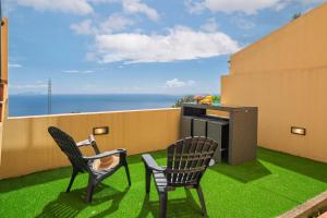 two chairs and a table on a balcony with green grass at Strategic Sunset House by An Island Apart in Santa Cruz