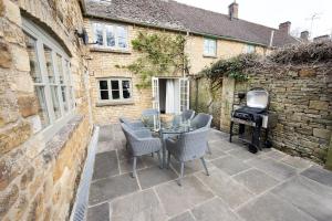 un patio avec une table, des chaises et un barbecue dans l'établissement The Perfumery Cottage, à Bourton-on-the-Water