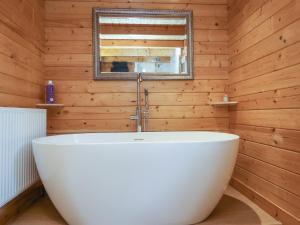 a white tub in a wooden bathroom with a mirror at Woodpeckers in Cullompton +26 photos