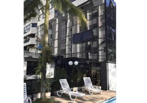 グアルジャにあるApto Aconchegante Piscina 2 Vagasの椅子2脚とヤシの木のある建物の画像