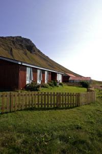 a fence next to a house with a hill in the background at Rauðsdalur in Brjánslækur