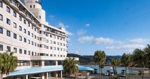a large white building with palm trees next to a river at Hotel SEASONS NICHINAN in Nichinan
