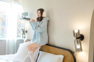 a woman standing on a bed holding a hair dryer at EUPHORIA丨Quiet Garden Quiet Designer Garden Hotel丨Datang Never Sleeps City Big Wild Goose Pagoda Subway Station Branch丨Near the scenic area in Xi'an