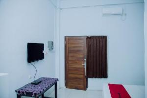 a room with a door and a bench and a television at RedDoorz at Hening Homestay in Montongbuwoh