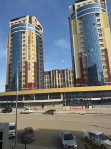 two tall buildings with cars parked in a parking lot at Байсанат 1 in Zhezdi