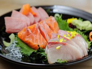 a black plate of food with fish and vegetables at HOTEL MYSTAYS Fuji Onsen Resort in Fujiyoshida +52 photos