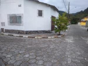 a white building with a tree next to a street at Quarto e Cozinha em Mongaguá in Mongaguá