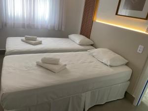 two beds in a room with white sheets and towels at Apartamento no centro da cidade in Serra Negra