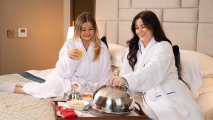 two women sitting on a bed with a tray of food at Europa Hotel in Belfast