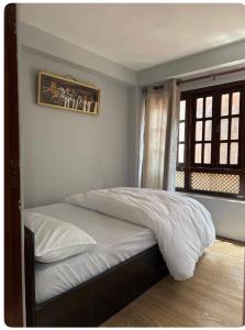a bedroom with a bed with white sheets and a window at The Locals bhaktapur in Bhaktapur +2 photos