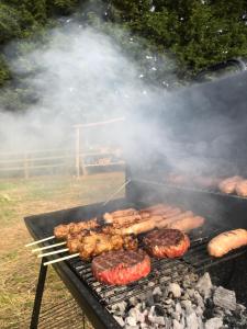 a grill with meat and hamburgers on it at Swallows Oast Glamping in Sedlescombe
