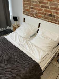 Una cama con sábanas blancas y almohadas junto a una pared de ladrillos. en Apartament Monstera II- top śniadanie, en Bydgoszcz