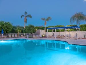 a large swimming pool with chairs and palm trees at Downtown Winner at Plaza Villas by ACME House Company in Palm Springs