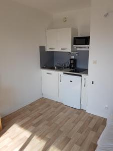 a small kitchen with white cabinets and a wooden floor at studio front de mer in Ouistreham