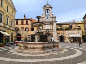 ein Brunnen mitten auf einer Straße mit einem Uhrturm in der Unterkunft Mad House Sutri Home Sweet Home Viterbo in Sutri