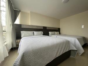 a bedroom with two beds with white sheets and a window at Hotel Iberia Plaza in Ipiales