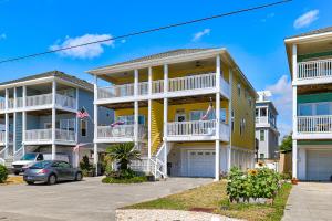 Una gran casa amarilla con balcones blancos en un estacionamiento. en Poopka & Dennys Beach Condo by Carolina Beach Realty, en Carolina Beach