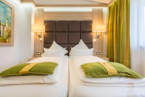 a bedroom with two white beds with green pillows at Best Western Plus Hotel Füssen in Füssen
