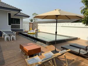 a pool with an umbrella and chairs and a table at The Wing Pool Villa Surin in Surin