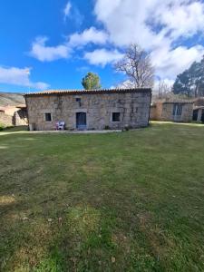Un edificio de piedra con un campo de césped delante. en La Serrota Casa Rural, en Navacepedilla de Corneja